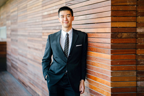 man in a suit leaning against a wooden wall